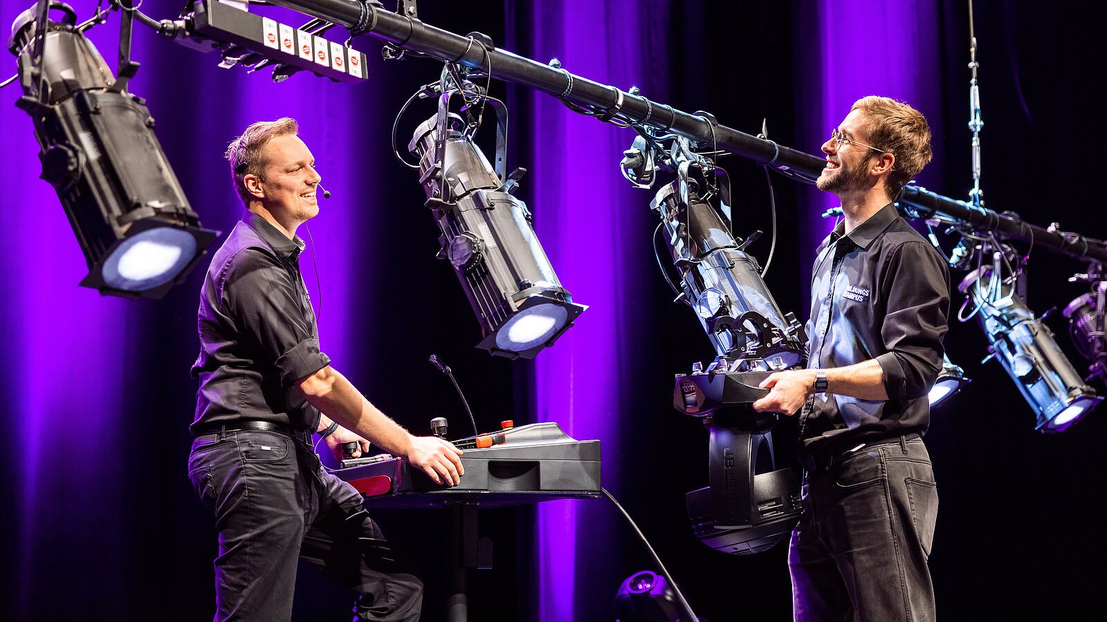 The photo shows two men working on spotlights in the Auditorium.
